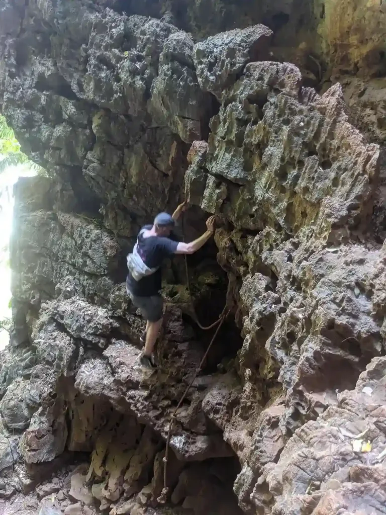 A hiking area that has a section in which hikers must do a small rock climbing section to proceed on the hiking path. This image shoes a person climbing a rock cliff, which has many spots for gripping with hands and mounting feet.
