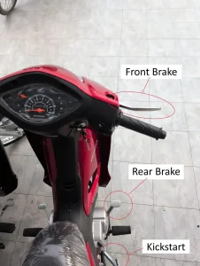 An image of a semi-automatic motorbike. There is text with arrows pointing at the controls of a semi-automatic motorbike. This image highlights the locations of the front brake (on handlebar right-hand side), rear brake (on right-hand side foot peg), and kickstart (behind the right-hand side foot peg).