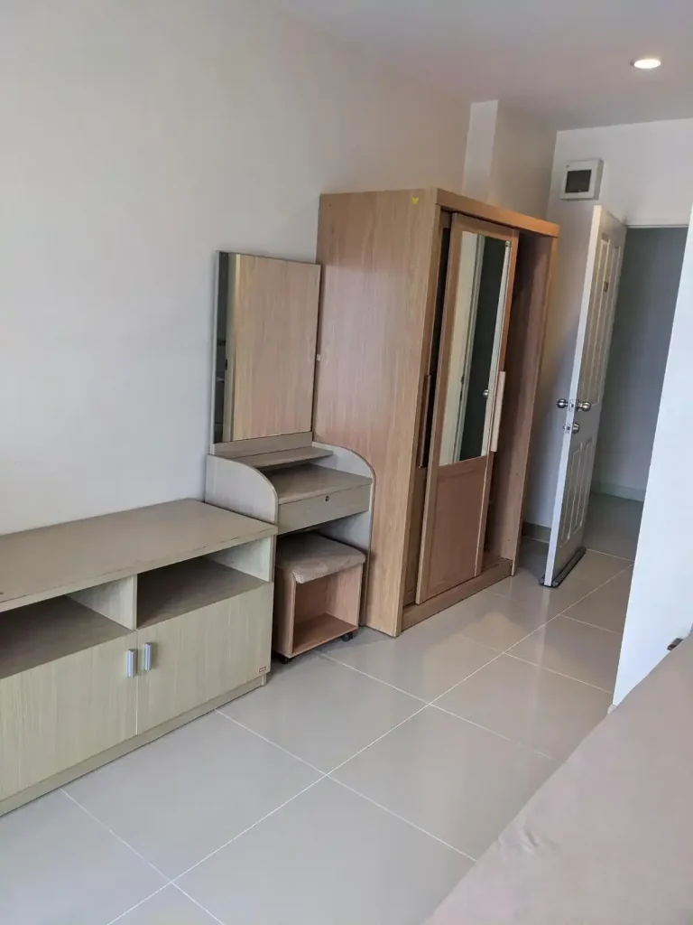 A furnished studio room rented monthly in Southeast Asia. The image shows the front door, a storage wardrobe, a small desk with mirror and chair, and an entertainment center with storage, but nothing on it. The floor is tile, which is very common in Southeast Asia.