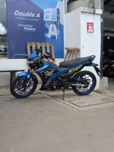 A parkedfully manual motorbike with a 150 cc engine size. This model is a Suzuki Satria, and is similar to a Honda Winner, both most common in Malaysia, but found throughout Southeast Asia.
