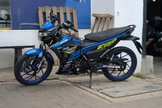 A parkedfully manual motorbike with a 150 cc engine size. This model is a Suzuki Satria, and is similar to a Honda Winner, both most common in Malaysia, but found throughout Southeast Asia.