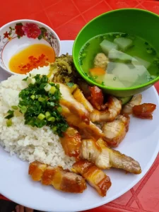 Thai stir-fried crispy pork on rice with sauce on the side. Included is a small simple soup with some vegetables inside. Crispy pork the meat as bacon, but small chunks instead of long thin slices. The meat has a thin batter on the edge, causing it to be crispy when fried.