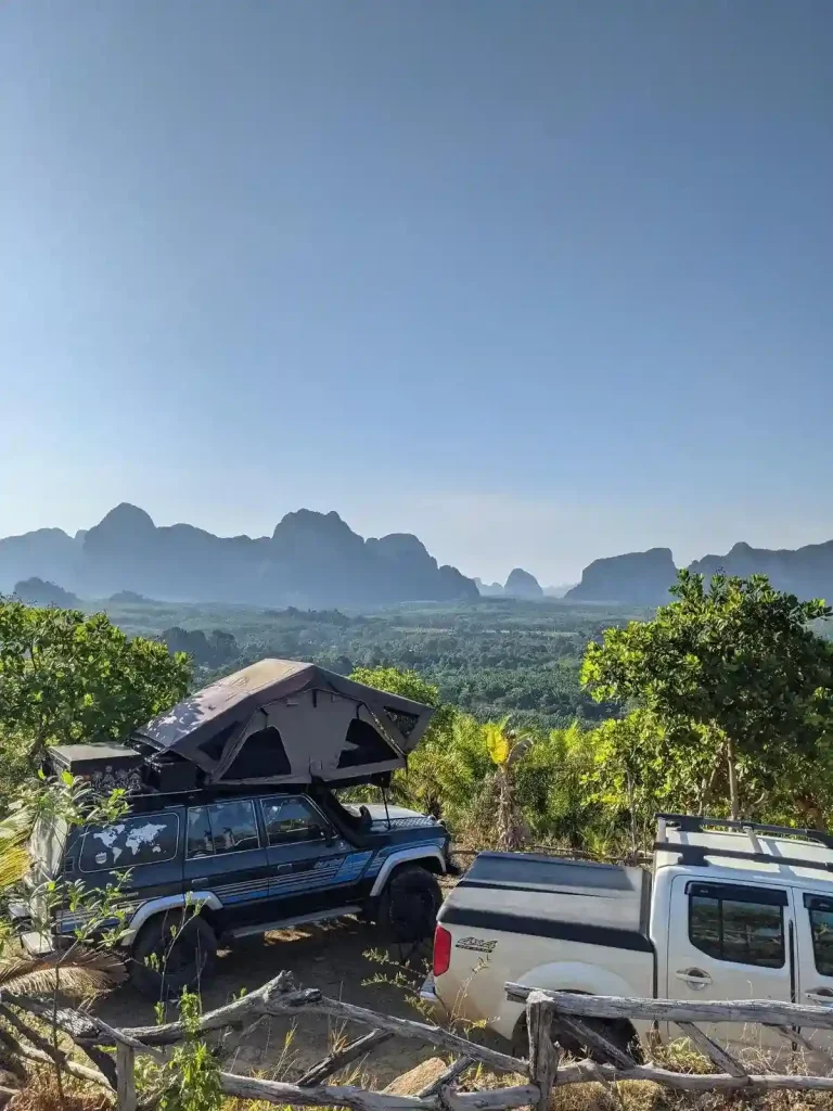 A parked Toyota Landcruiser with a camping tent setup on it's roof. This is a camping spot surrounded by mountains and palm trees (a palm oil plantation) at Kuan Nom Saow Restaurant and Viewpoint in Krabi Thailand.