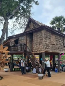 A traditional wooden house in Cambodia. The home is a stilt house, meaning it is elevated off of the ground. The house is framed using wood. The roof, walls, and windows are made of straw. Because it is a stilt house, there are stairs leading up to the home (second floor) with a deck where the front door is located. Below is empty, but often used for storage.