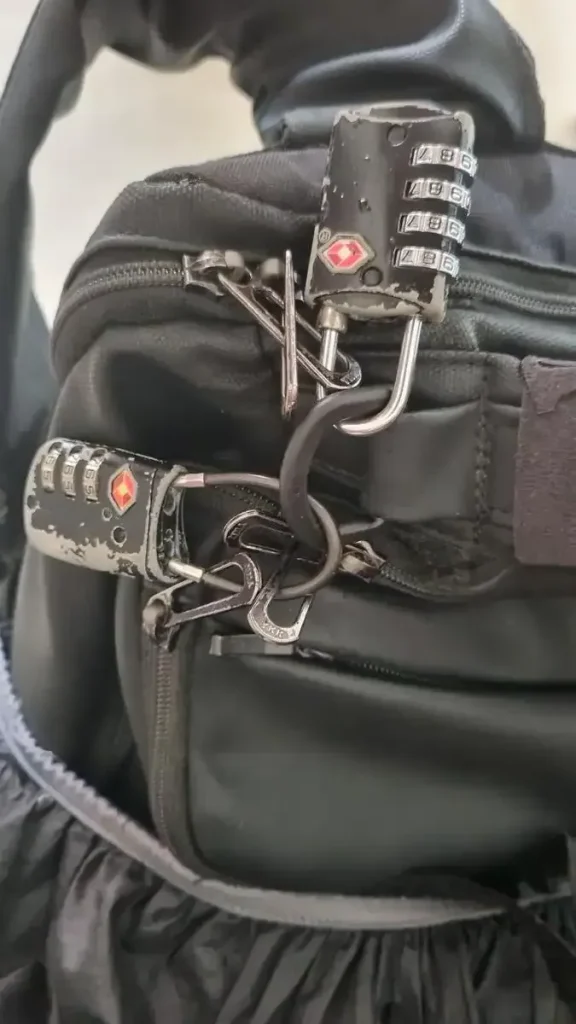 2 TSA travel locks on travel bag, locking 3 bag compartments to prevent theft. One lock has a metal shackle that is rigid, the other has a braided cable shackle that is flexible.