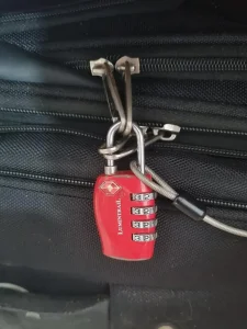 TSA travel lock on travel bag. The lock is looped through 2 pairs of zippers. Also, the end loop of a metal travel cable is attached to the lock in order to achor it to an anchor object to prevent theft.