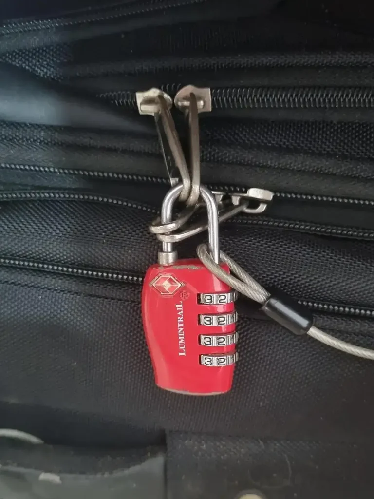 TSA travel lock on travel bag. The lock is looped through 2 pairs of zippers. Also, the end loop of a metal travel cable is attached to the lock in order to achor it to an anchor object to prevent theft.