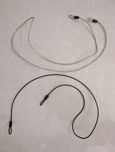 Two travel tether cables, stretched out and laying on the floor for display. These are to tether and lock something (usually a backpack or luggage) to an anchor object such as a heavy bed frame that cannot be moved. These cables are made of braided steel, and covered with rubber. The ends have loops for hooking a lock onto them. The loops are comprised of folding the end of the cable, and crimping the cable together to form a loop. These cables are very strong.