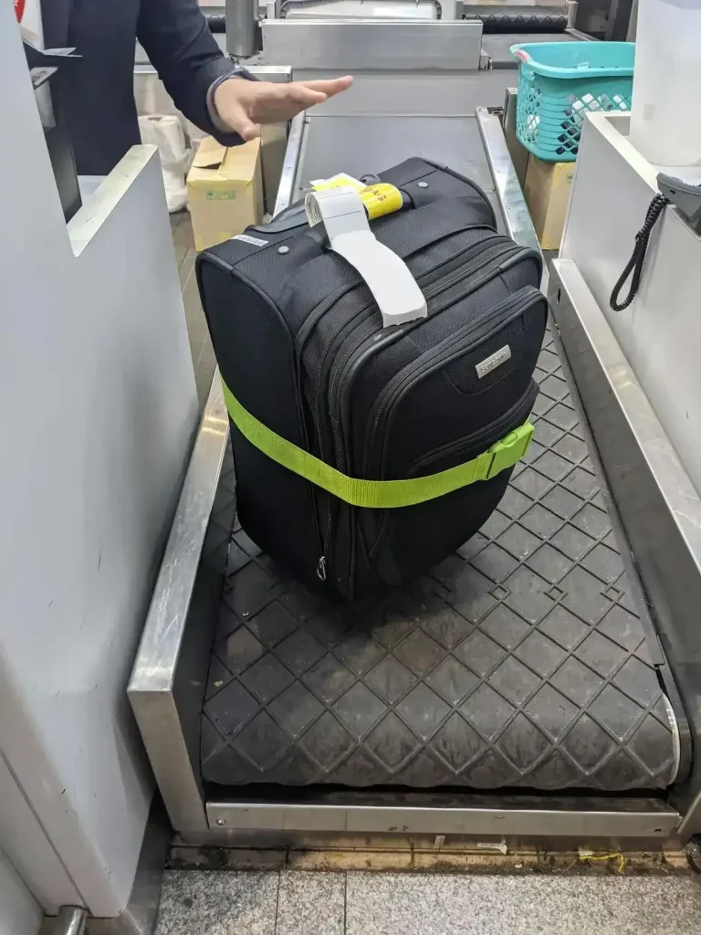 A check-in luggage bag being weighted at an airport airlines check-in counter. The bag has a baggage belt to compress the bag, and to act as a flag so that the owner knows it is theirs when reclaiming it at the final destination's luggage rack.