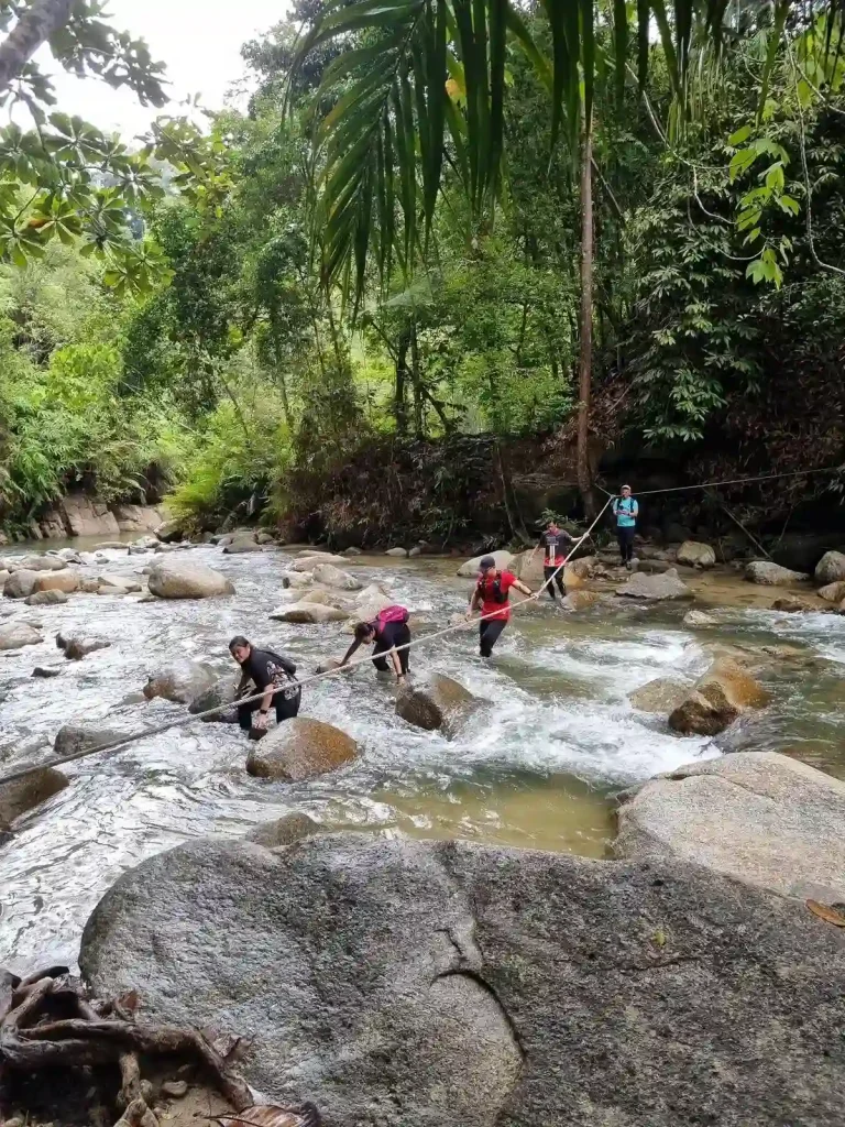 Wet adventures. Hiking through knee-deep water rapids in the jungle of Malaysia. The rapids has many rock boulders, and a rope connected to trees on each side for hikers to hold onto when crossing the rapids.