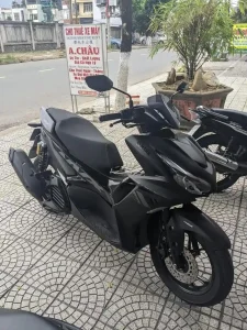 A Yamaha NMAX 155cc automatic motorbike in Vietnam. The motorbike is parked on a sidewalk along the road in front of a café.