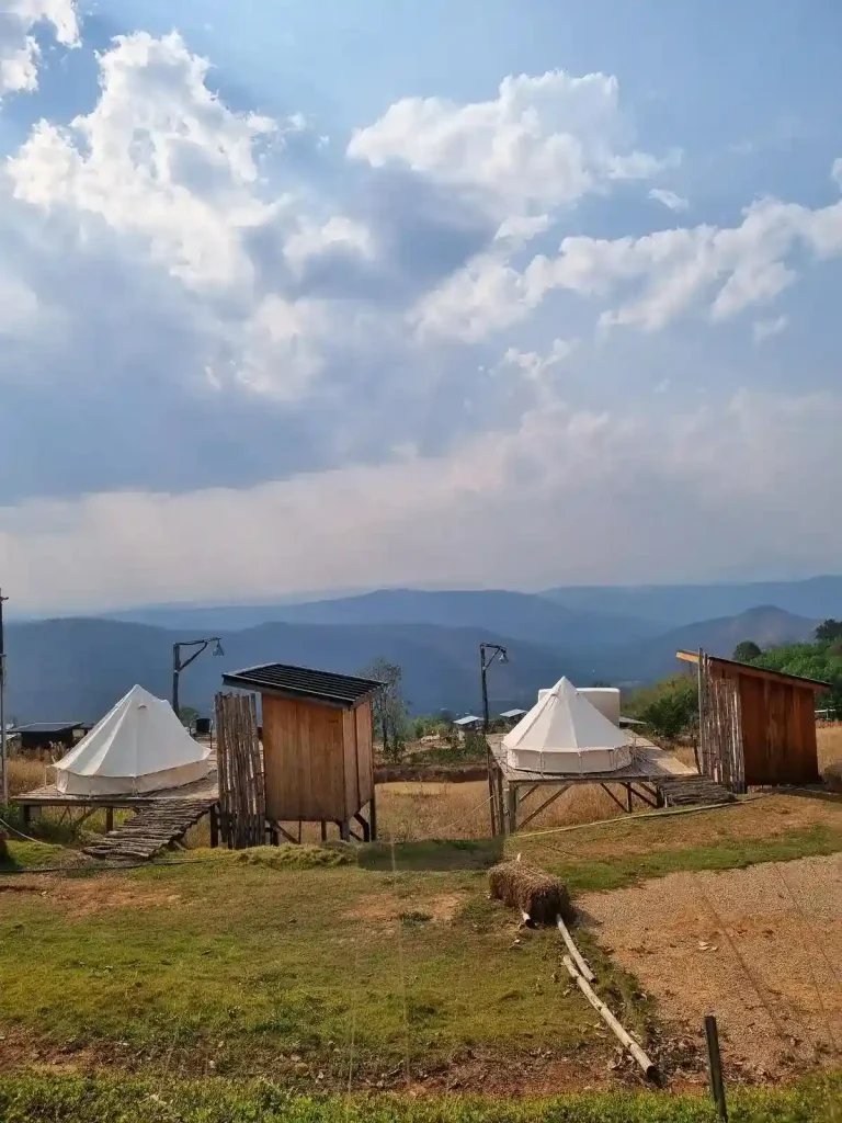 Two camping spots next to each other, each with a canvas yurt (a style of tent) and an outhouse bathroom. The spot is ontop of an elevated area in the region, overlooking a mountainous area with a valley in between the spot and the mountains.