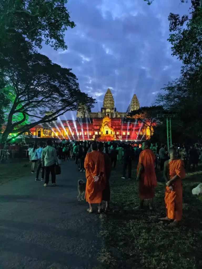 Night time with lights at Angkor Wat for the Angkor Thanksgiving show, which is a yearly celebration for the inclusion of Angkor Wat as a UNESCO world heritage site. There is a stage at the East side of Angkor Wat with several spot lights as well as colored lighting. There are three Buddhist monks in saffron robes in the foreground near the photographer. These robes are called Kasaya, which is a monk's robe colored in saffron dye.