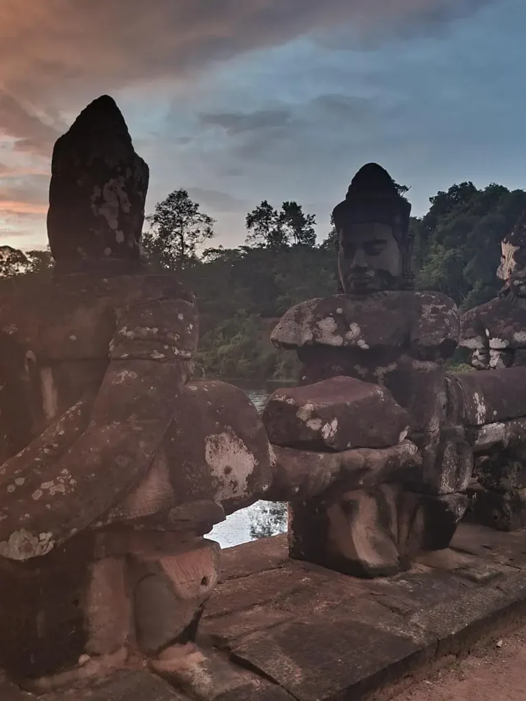 A close-up of the stone statues allong the Angkor Thom south gate. These are individual statues of men pulling a long naga serpent. The naga serpent spans the entire length of the bridge, and the individual men are attached to the naga, at about a meter and a half (five feet) apart. This image shows only two of those male statues.