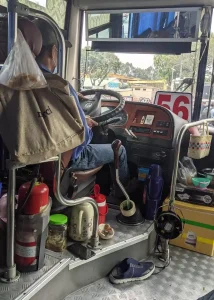 A bus driver in Vietnam driving barefoot. His shoes can be seen on the floor and his bee barefoot. The heel of his shoe is compressed - it seems as if he wears them as slip-ons.