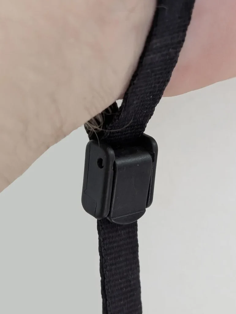 This is a close-up of the locking clip on the Blackrapid-brand short leash that is tethered & locked onto a person's hand / wrist. It is meant to show how the leash is securely clipped & attached to the wrist. The hand was fed through the tether, the lock clip was tightened, and then the locked clip was set to the locked position around the person's wrist. Since the leash has a quick-attach hook (similar to a rock climbing clip) on the other end, the leash is clipped onto the tether tab mounted on the cellphone (not shown). The cellphone (not show) is hanging from the person's wrist to display this leash tether system. The benefit is to show how the phone cannot be accidently dropped or stole out of your hand - the leash tether system keeps it securely attached to the hand / wrist.
