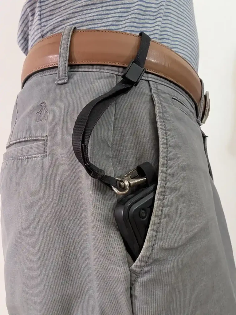The Blackrapid-brand tether tab and short leash combo tethered & locked onto a pants belt. The belt was fed through the tether, the lock clip was tightened, and then the locked clip was set to the locked position. Since the leash has a quick-attach hook (similar to a rock climbing clip) on the other end, the leash is clipped onto the tether tab mounted on the cellphone. The cellphone is sticking out of the pants pocket to display this leash tether system, but the leash is just long enough for the phone to go completely into the pants pocket. The benefit is to show how the phone cannot be pickpocketed - the leash tether system keeps it securely attached to the hip (the pants belt).