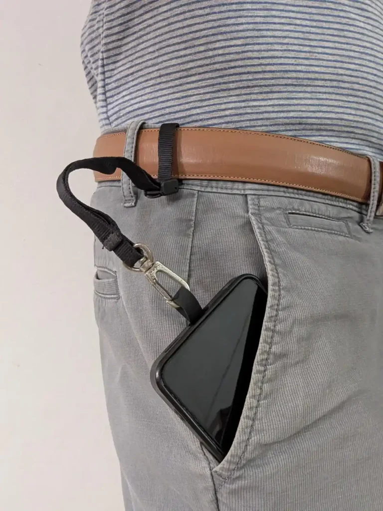 The Blackrapid-brand tether tab and short leash combo tethered & locked onto a pants belt. The belt was fed through the tether, the lock clip was tightened, and then the locked clip was set to the locked position. Since the leash has a quick-attach hook (similar to a rock climbing clip) on the other end, the leash is clipped onto the tether tab mounted on the cellphone. The cellphone is sticking out of the pants pocket to display this leash tether system, but the leash is just long enough for the phone to go completely into the pants pocket. The benefit is to show how the phone cannot be pickpocketed - the leash tether system keeps it securely attached to the hip (the pants belt).