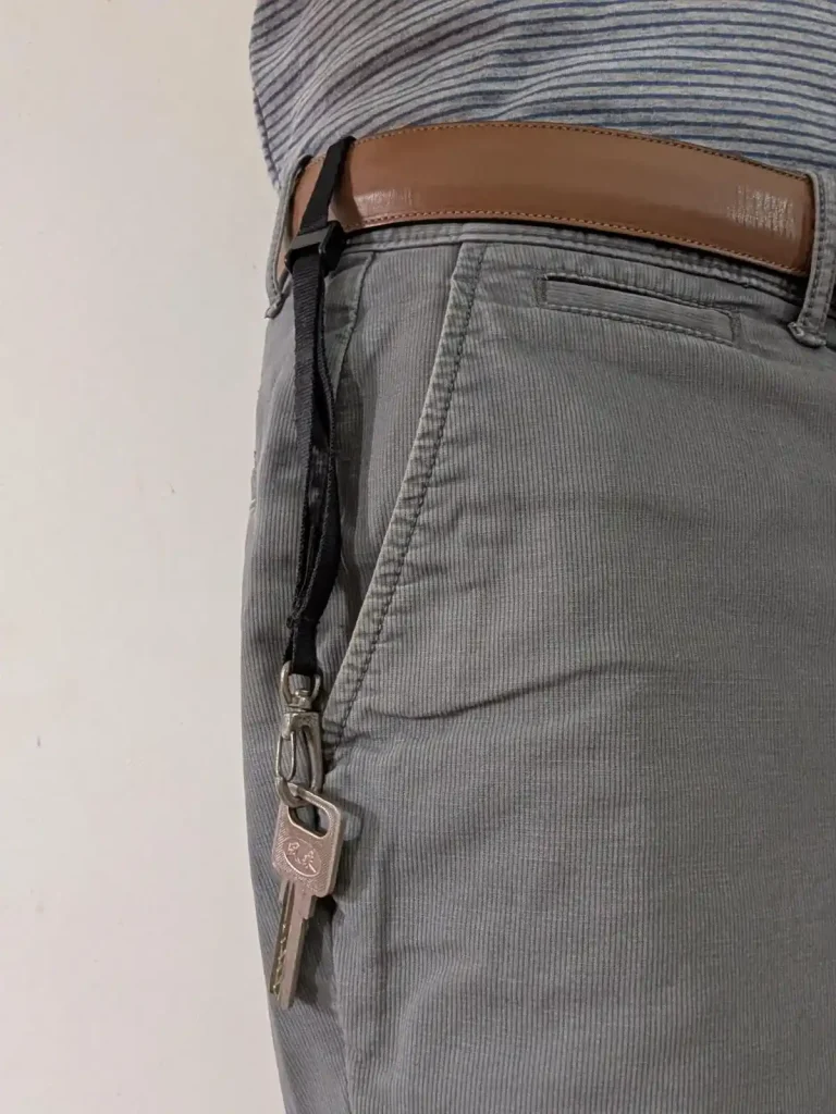 The BlackRapid-brand short leash tethered & locked onto a pants belt. The belt was fed through the tether, the lock clip was tightened, and then the locked clip was set to the locked position. Since the leash has a quick-attach hook (similar to a rock climbing clip) on the other end, a key is clipped onto the leash. The key is sticking out of the pants pocket to display this leash tether system, but the leash is just long enough for the key to go completely into the pants pocket. The benefit is to show how the key cannot be lost - the leash tether system keeps it securely attached to the hip (the pants belt).
