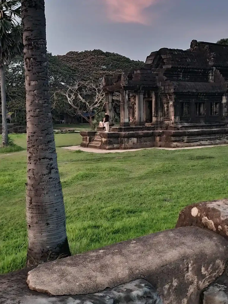 A building within the grounds of the Angkor Wat complex. There are two people, a male and female, resting on the steps of this small building. This is located within Angkor Archaeological Park, which is a UNESCO World Heritage Site.