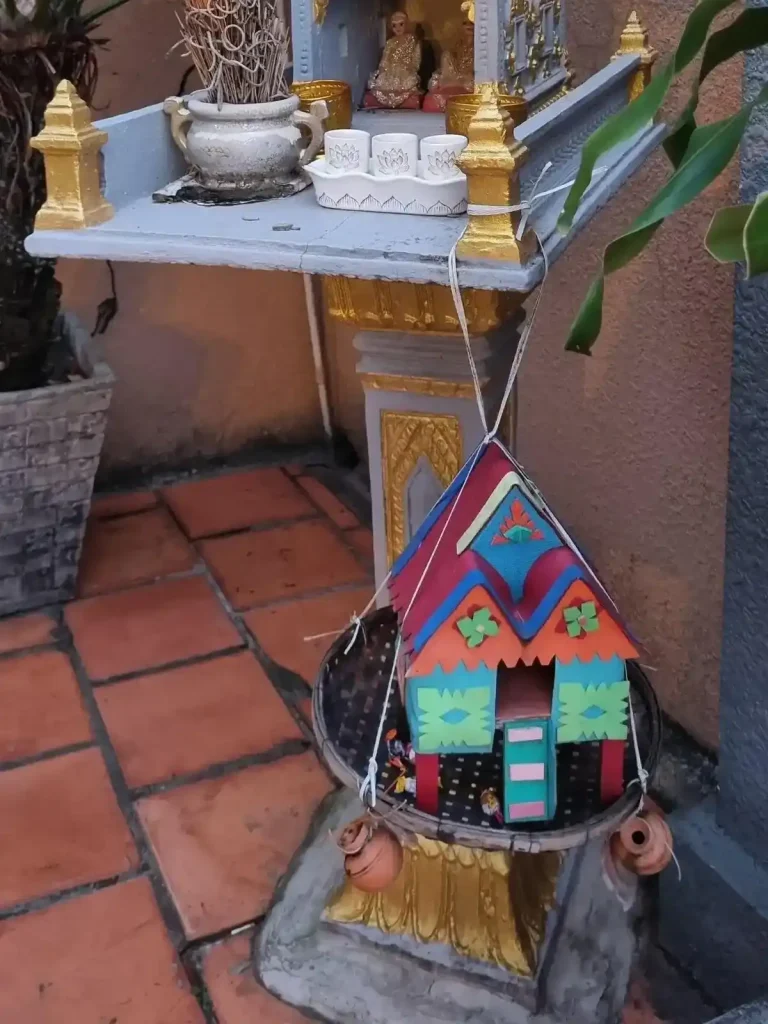 A close-up of a small child-version spirit house hanging from a larger, main, spirit house.