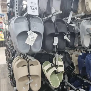 Pairs of classic simple sandals of various color and styles on a rack, for sale in a store in Thailand. One pair has a price of one hundred and twenty-nine Thai Baht (about four dollars and twenty-five US cents).