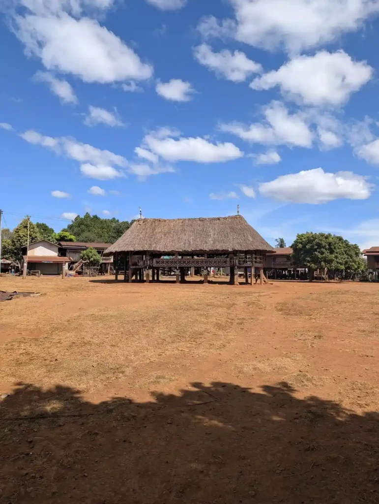 A communal center, which is a hut, in a small village in Laos. The hut has a straw roof, and is constructed in the style of a stilt house method. The stilts are wooden beams (tree trunks) that are driven vertically into the ground. These beams are the support structure for a horizontal platform is constructed.