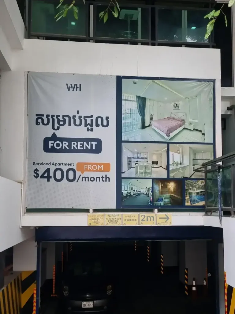 A for rent sign for a serviced apartment in Cambodia. The pricing at this building starts at four hundred US dollars per month. On the sign, there are pictures of the room, kitchen, gym, sauna, and pool. This is a fully furnished rental.