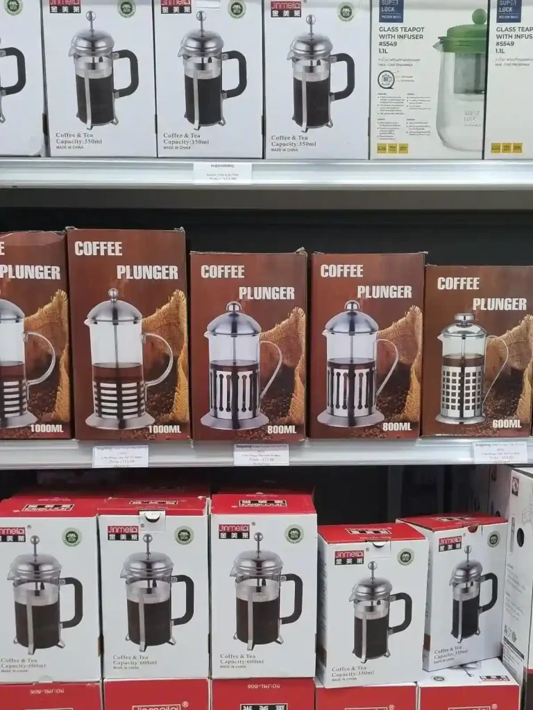Six different French Press coffee plungers for sale at a grocery store in Southeast Asia. Some are large-size, others are smaller-size. Prices are between ten and fourteen US dollars.