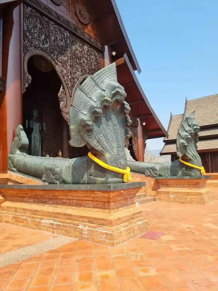 A wooden temple with two jade naga (a mythical snake-like creature with seven heads combined as one) statues at the entrance of the temple. Each naga statue stands at about six feet tall (1.8 meters). The naga has a long body.