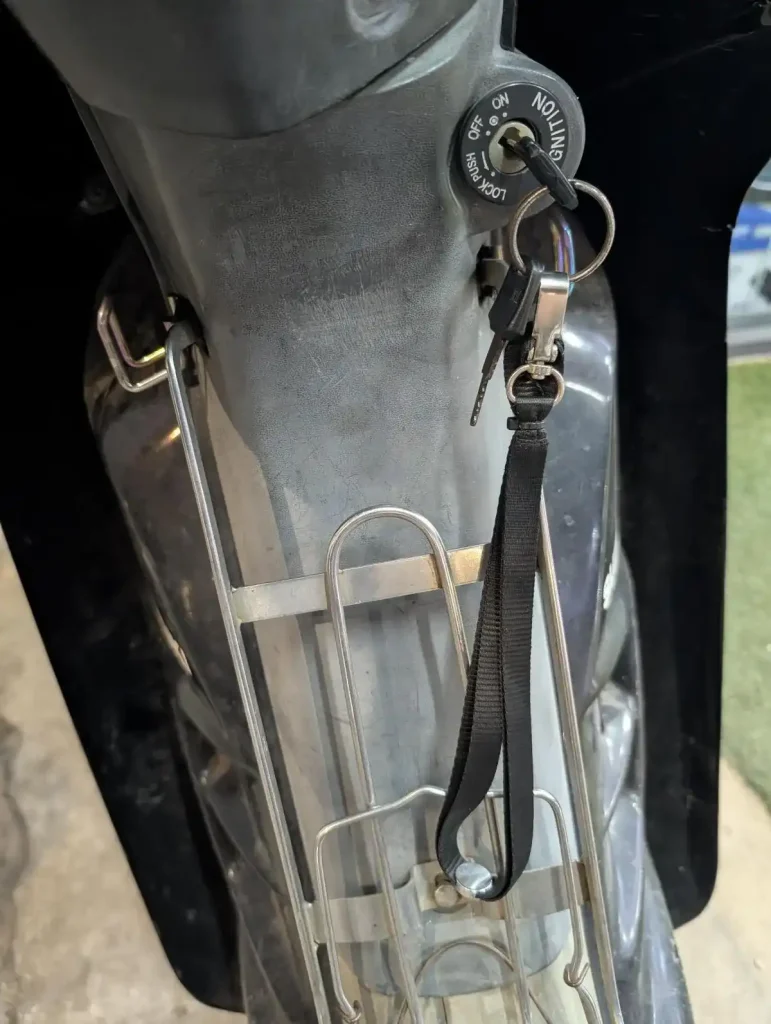 A lanyard with motorbike keys attached to it. The motorbike key is in the ignition of a motorbike, and the lanyard leash is dangling.