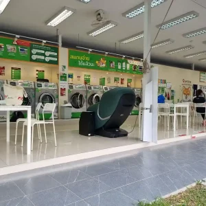 A laundromat with washing and drying machines in Southeast Asia. There are a few desks with chairs. Also, there is a well-padded massage chair for use. People take off their shoes when entering. The laundromat is open-air on two sides. The other two sides have wall where the machines are mounted. There is a roof covering the building and entrance.