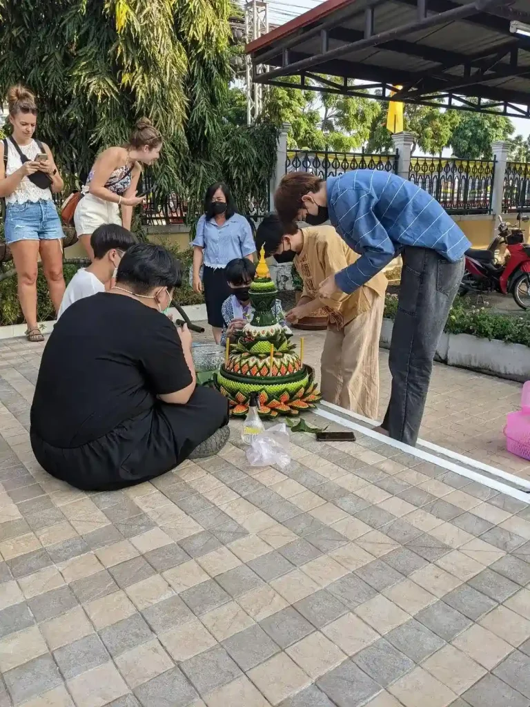 A few Thai people making a large krathong during the Loi Krathong holiday in northern Thailand. It is mostly finished, but they are adding some finishing touches to it. It basically looks like a stupa made of flowers and banana leaves folded in intricate patterns.