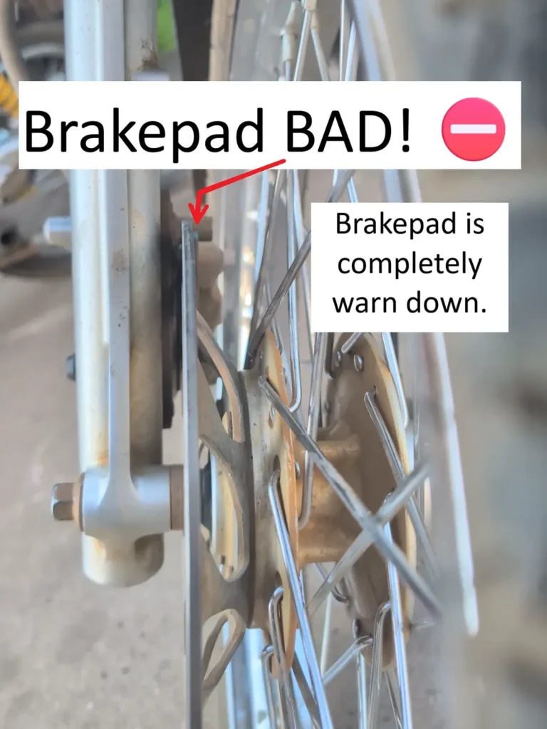 A bad front brake pad on a motorbike. The image has arrows pointing to show how the brake pad is worn down. This is not good (not safe) and needs to be replaced as soon as possible. This brake pad is on the front wheel of a motorbike (a.k.a. scooter, motorcycle).