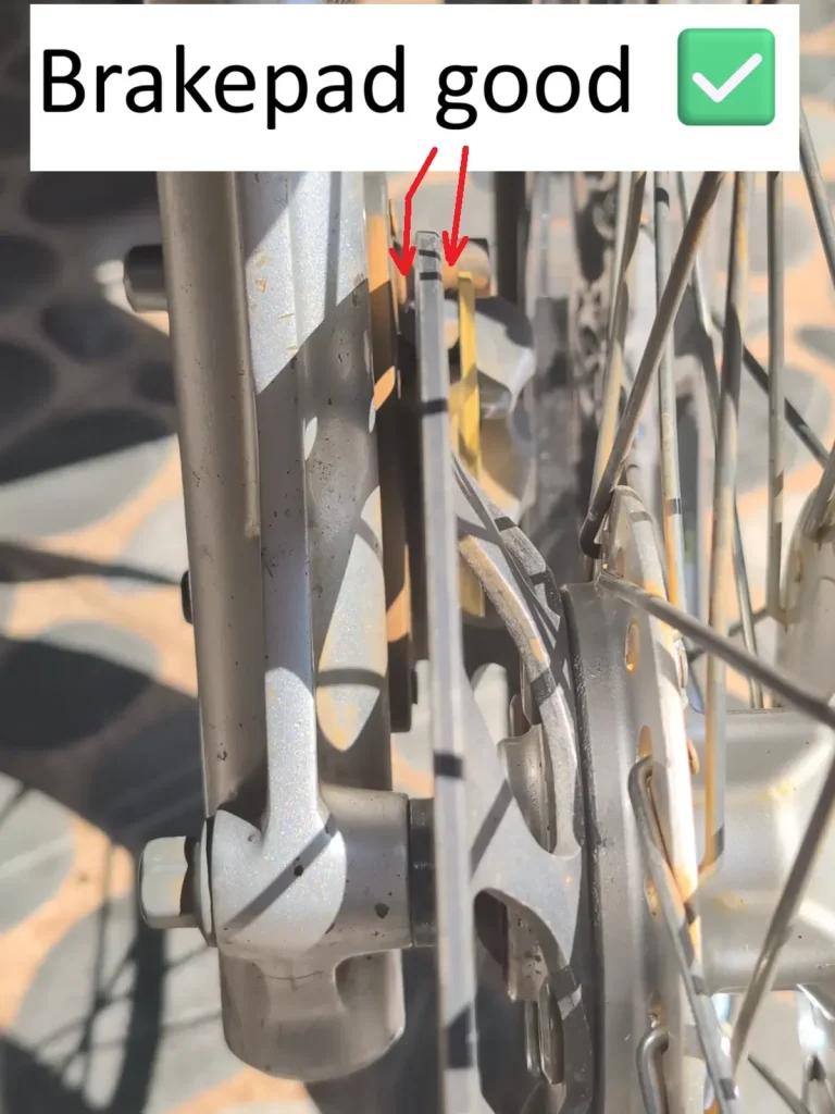 A good front brake pad on a motorbike. The image has arrows pointing to show how the brake pad is good! There is lots of brake pad remaining, and is safe to ride! This brake pad is on the front wheel of a motorbike (a.k.a. scooter, motorcycle).