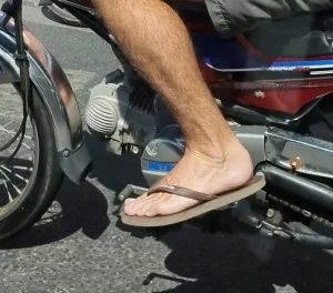 A motorbike (scooter) rider in Southeast Asia wearing flip flops. This image is a close-up of the rider's left foot and sandal on the footpeg of a Detech Honda Win motorbike.