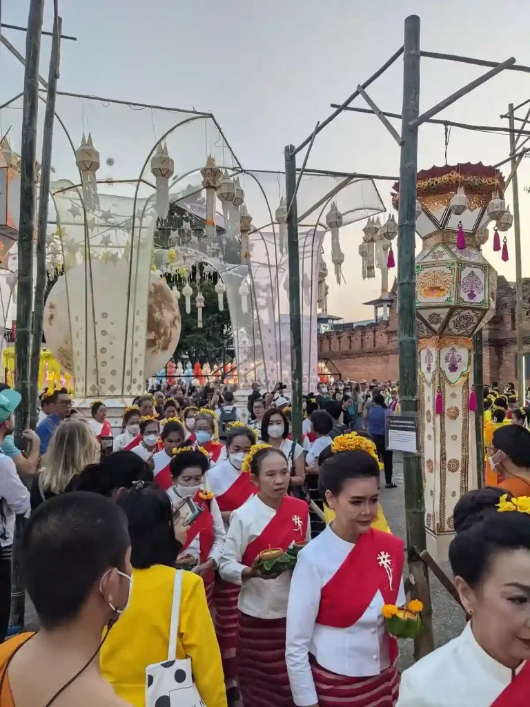 Women in a traditional Thai clothing are walking in a parade that celebrates the Lantern festival (Yi Peng holiday) in northern Thailand. Several unique and difficult-to-describe lanterns surround the area.
