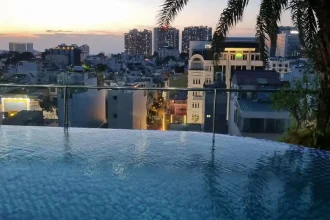 Viewing a sunset from a rooftop infinity swimming pool in Southeast Asia. High rises can be seen between the pool and the sunset, since this takes place in a large, densely populated, city in Southeast Asia.