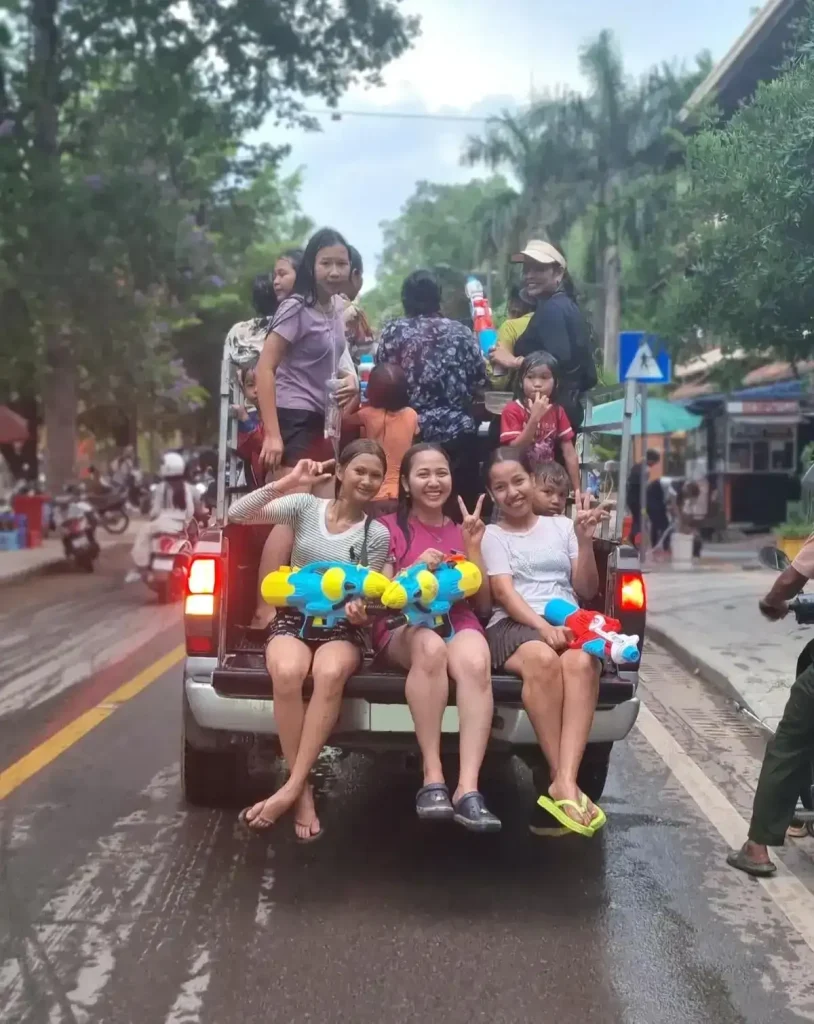 Thirteen females of all ages with water guns in the back of a pickup truck bed. This is during the Songkran holiday festival in Cambodia. This festival is essentially one massive water fight, and everyone gets soaking wet.
