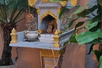 A spirit house with burned incense. There is a small child-version spirit house hanging from the main spirit house.