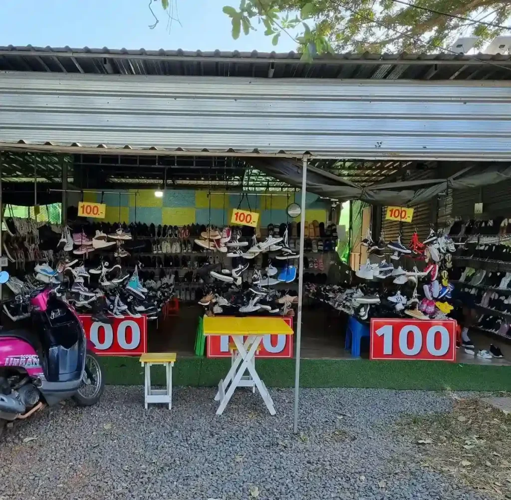 A store selling used shoes in Thailand. There are signs with the number one hundred, implying the price of three US dollars, or one hundred Thai Baht.