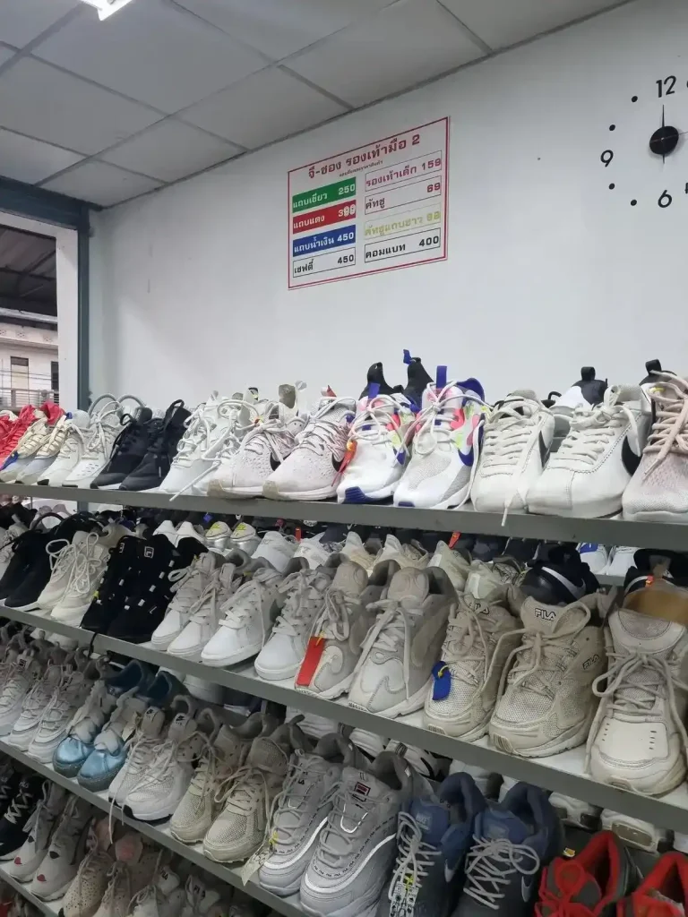 A store selling used shoes in Thailand. This image shows a rack of used shoes, including several pairs of name brand Nike shoes in good condition. There is a sign on the wall that references pricing between two hundred fifty Thai Baht (about eight and a half US dollars), to four hundred fifty Thai Baht (about fifteen US dollars).