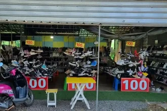 A store selling used shoes in Thailand. There are signs with the number one hundred, implying the price of three US dollars, or one hundred Thai Baht.