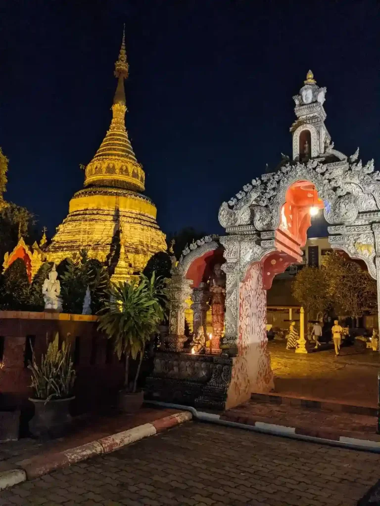A temple complex in Chiang Mai, Thailand that has a large stupa, which has a light shining on it during the night when it's dark.