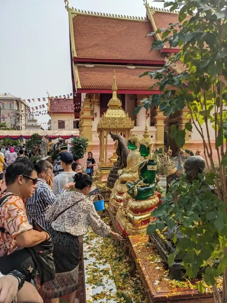 Lao people at a temple complex splashing a jade buddha statue with water. This is during the Songkran holiday, in which splashing each other (and the buddha statue in this case) with water is a spiritual act that signifies cleansing during this holiday. While the fun water fight aspect of the holiday has become commercialized as a fun thing to do, the people at the temple are taking splashing the buddha seriously.