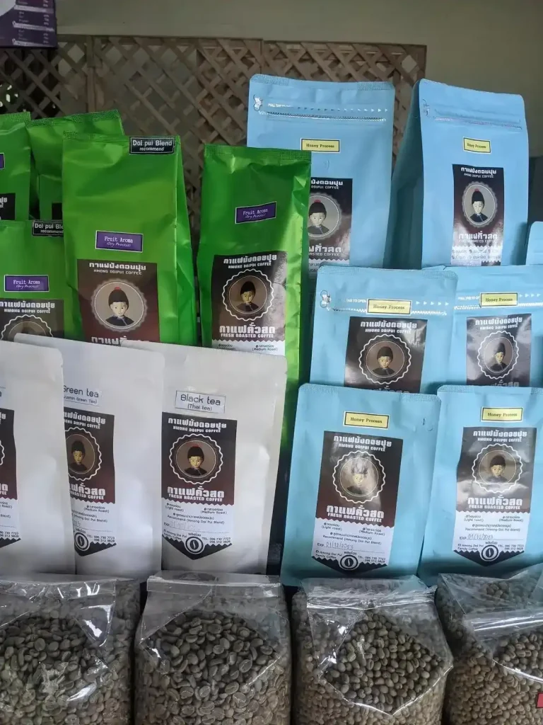 Bags of coffee beans for sale in Thailand. The brand is Hmong Doipui coffee, from the Doipoi region in norther Thailand. There a few different roasts - "Fruit Aroma (Dry processed)" and "Medium Roast Honey processed". There is also a "Black Tea (Thai tea)". There are also coffee beans in clear see-through plastic with no labeling on them.